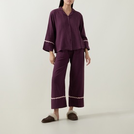 Model wearing Their Nibs Fig Baby Wavy-Trim Pyjama Set in fig, with white wavy trim at cuffs and hems, styled with brown slippers