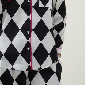 Model wearing Their Nibs pyjama shirt in cream and black harlequin diamond print with pink contrast piping and button front.