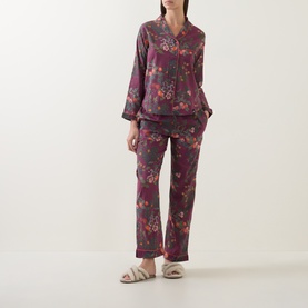 Model wearing Their Nibs plum floral cotton pyjama set with long sleeves and straight-leg trousers, styled with fluffy sliders