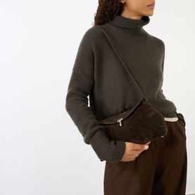 Model carrying Toteme T-Lock Suede Clutch in brown suede, worn crossbody with silver-tone hardware, styled with dark knit and tailored trousers