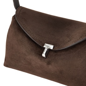 Toteme T-Lock Suede Clutch in brown with silver-tone T-lock flap closure, removable black shoulder strap visible above