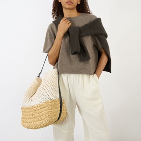 Model carrying Toteme Belted Raffia Tote Bag in ecru/vanilla, dual-toned raffia, leather belt strap, silver-tone hardware, styled with grey knit top