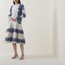 Model wearing Ulla Johnson Carina Jacquard Cardigan in Lapis, blue leaf jacquard pattern, with a flared midi skirt and nude heeled mules.
