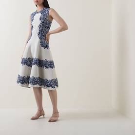 Model wearing Ulla Johnson dress in Lapis, sleeveless fit-and-flare silhouette with navy floral appliqu&eacute; border detail on white fabric