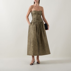 Model wearing Ulla Johnson Lumina Textured Gown in Light Gold, strapless ruched bustier, flared midi skirt, styled with black clutch and mules