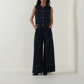 Model wearing Ulla Johnson Tigris jumpsuit in dark indigo denim, sleeveless, wide-leg silhouette with contrast stitching and button details