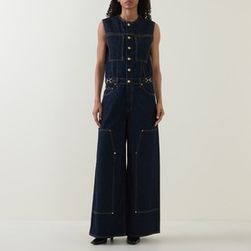 Model wearing Ulla Johnson Tigris denim jumpsuit in dark indigo, sleeveless with button front, contrast stitching and wide-leg fit