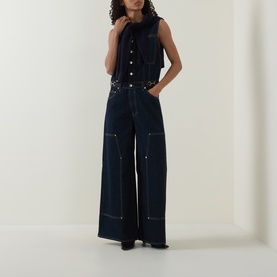 Model wearing Ulla Johnson Tigris jumpsuit in dark indigo denim, sleeveless, wide-leg silhouette with contrast stitching and gold button details
