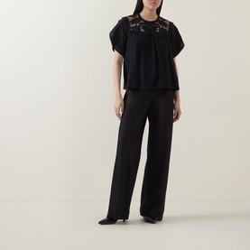 Model wearing Ulla Johnson Alma Embroidery Lace Silk Top in Noir with wide-leg black trousers and black heels.