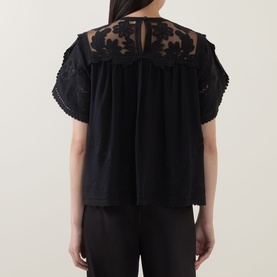 Model wearing Ulla Johnson Alma Embroidery Lace Silk Top in Noir, back view showing floral embroidered tulle yoke, short sleeves, button keyhole