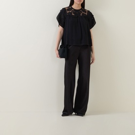Model wearing Ulla Johnson Alma Embroidery Lace Silk Top in Noir with black wide-leg trousers and pointed heels.