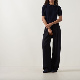 Model wearing Ulla Johnson Jude Embellished Top in Midnight, with embellished round neckline and short sleeves, styled with wide-leg black trousers.