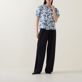 Model wearing Ulla Johnson Amaria Layered Stripe Top in Ciel with puffed sleeves and ruffle collar, styled with wide-leg black trousers