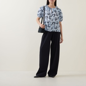 Model wearing Ulla Johnson Amaria Layered Stripe Top in Ciel with puffed sleeves and floral print, styled with black wide-leg trousers and shoulder