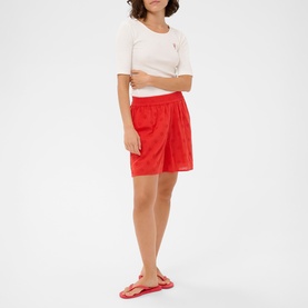 Model wearing Kaffe Poppy Red shorts with elasticated waist, styled with a cream crop top and red flip-flops