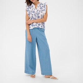 Model wearing Kaffe Chalk Midnight Flower floral print sleeveless top with wide-leg light blue denim trousers and white sandals.
