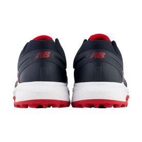 New Balance cricket shoes in navy and red, shown from rear angle, white midsole, rubber studded outsole