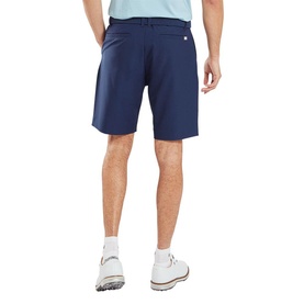 Model wearing Footjoy navy golf shorts, rear view, styled with white golf shoes and light blue top.