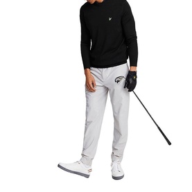 Model wearing grey slim-fit golf trousers, styled with black long-sleeve top and white trainers, holding a golf club and cap