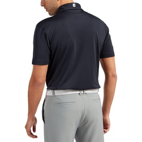Model wearing FootJoy navy short-sleeve polo shirt, back view, styled with light grey trousers and white belt