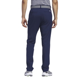 Model wearing navy blue Adidas slim-fit golf trousers, rear view, styled with a striped polo shirt and white golf shoes.