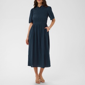 Model wearing Kaffe midi dress in Midnight Marine, featuring short puff sleeves, smocked waist, and full skirt, styled with nude sandals