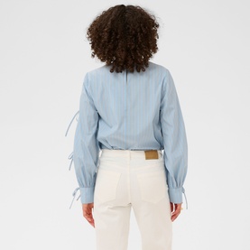 Model wearing Kaffe chalk blue striped long-sleeve blouse with tie cuffs, styled with white wide-leg trousers. Rear view.