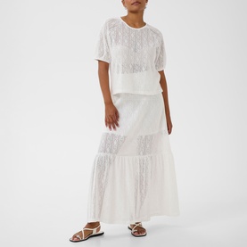 Model wearing Kaffe chalk white lace-textured top and tiered maxi skirt set, styled with strappy flat sandals