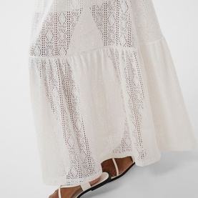 Model wearing Kaffe chalk white broderie anglaise tiered maxi skirt, styled with tan flat sandals