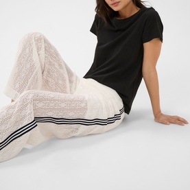 Model wearing Kaffe chalk crochet wide-leg trousers with black side stripes, styled with a black T-shirt, seated pose.