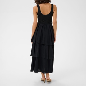 Model wearing Kaffe black deep tiered midi dress with ruched bodice, styled with silver heeled sandals, back view