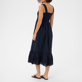 Model wearing Kaffe Midnight Marine midi dress with broderie anglaise hem, ruched bodice and tie straps, styled with black flat sandals