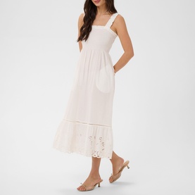 Model wearing Kaffe chalk midi dress with square neck, wide straps, smocked bodice, broderie anglaise hem, and side pocket. Styled with nude heeled