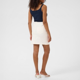 Model wearing Kaffe chalk mini skirt, styled with a navy tank top and white strappy heeled sandals, rear view