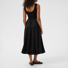 Model wearing Kaffe black deep midi dress with scoop back, full skirt and fitted bodice, styled with black flat shoes