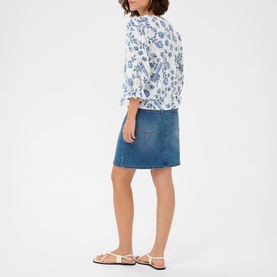 Model wearing Kaffe Chalk Midnight flower blouse with blue floral print, paired with denim mini skirt and white flat sandals