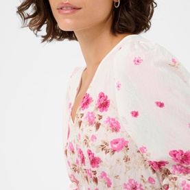 Model wearing Kaffe dress in White Rose Border Flower, featuring pink floral print, V-neckline and puff sleeves in lightweight fabric.