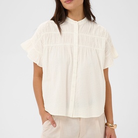 Model wearing Kaffe chalk short-sleeve blouse with pintuck and ruffle details, styled with beige trousers and gold bracelet.