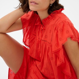 Model wearing Kaffe dress in Poppy Red with broderie anglaise detail, ruffle neckline, and flutter sleeves