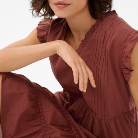 Model wearing Kaffe dress in Henna, featuring ruffle trim neckline, pintuck bodice detail and short frill sleeves in cotton fabric