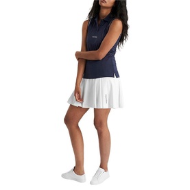 Model wearing Calvin Klein Golf navy sleeveless polo shirt with white pleated mini skirt and white trainers.