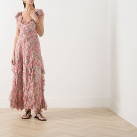 Model wearing Rixo Butterfly Paisley Orange silk maxi dress with ruffle trim, V-neck and flutter sleeves, styled with strappy flat sandals