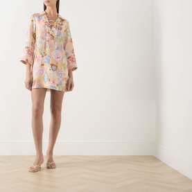 Model wearing Rixo Bloom Yellow floral mini dress with lace-up neckline and bell sleeves, styled with strappy flat sandals