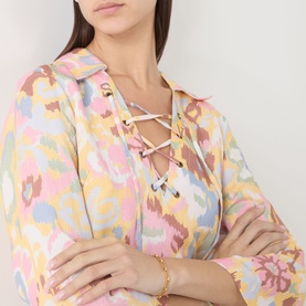 Model wearing Rixo dress in Bloom Yellow abstract ikat print with lace-up neckline, styled with gold chain bracelet and necklace.