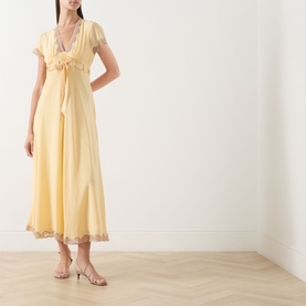 Model wearing Rixo butter yellow silk midi dress with lace trim, cap sleeves and tie front detail, styled with strappy heeled sandals.