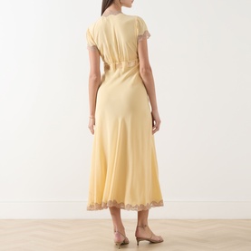 Model wearing Rixo Butter Yellow silk midi dress with lace hem trim and short sleeves, shown from behind with nude heels