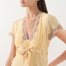 Model wearing Rixo Butter Yellow silk dress with lace trim neckline and sleeves, satin bow waist detail, pleated bodice