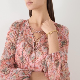 Model wearing Rixo dress in Cara Bandana Orange paisley print, styled with a gold chain bracelet and necklace.
