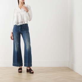 Model wearing Rixo Lilly Embroidery Ivory cotton top with wide-leg blue jeans and brown platform clogs.