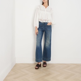 Model wearing Rixo Lilly Embroidery Ivory cotton top with wide-leg blue jeans and brown wooden mule sandals.